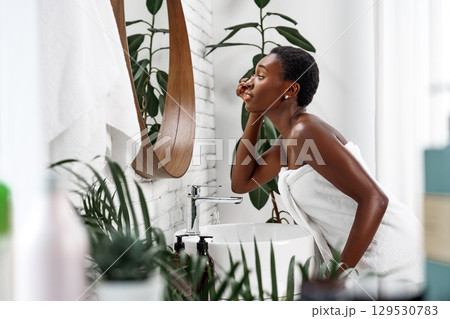 Woman applies skin care product at modern bathroom sink with lively greenery in the background during morning routine 129530783