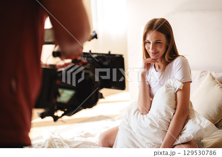 Model poses playfully during a photoshoot session in a sunlit bedroom setting with soft bedding Model poses playfully during a photoshoot session in a sunlit bedroom setting with soft bedding 129530786