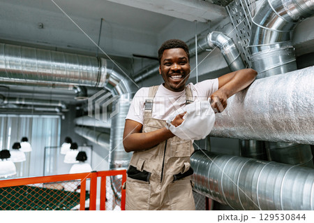 Maintenance worker smiling while taking off safety hat in an industrial setting during daytime hours 129530844
