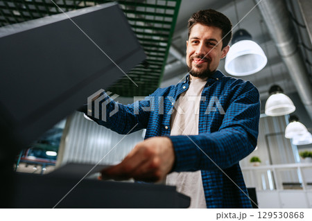 Man efficiently using a printer in a modern office environment during daytime hours Man efficiently using a printer in a modern office environment during daytime hours 129530868