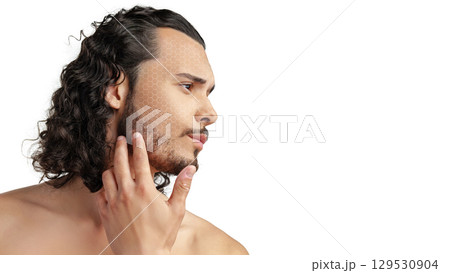 Man with curly hair touching his jawline while looking thoughtfully to the side in a minimalist setting 129530904