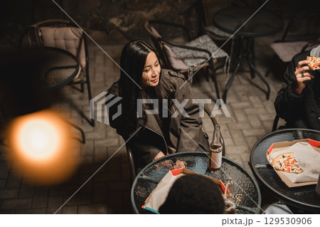 Group of friends enjoying food and drink outside at night in a cozy atmosphere 129530906