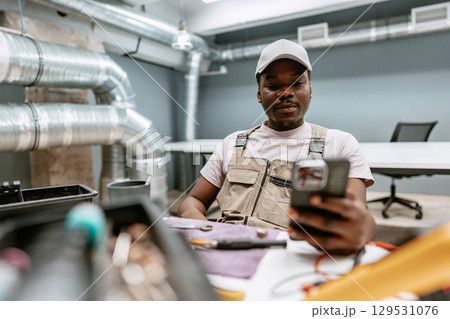 Skilled worker checking smartphone while seated in a modern workspace with exposed ductwork Skilled worker checking smartphone while seated in a modern workspace with exposed ductwork 129531076