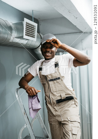 Worker smiling while standing on a ladder in a modern workspace during the day 129531091