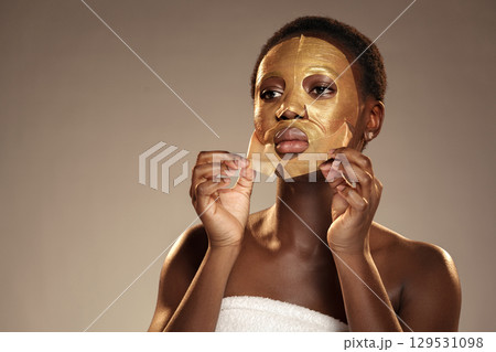 Woman applies a golden sheet mask in a skincare routine at a studio during a daytime session 129531098
