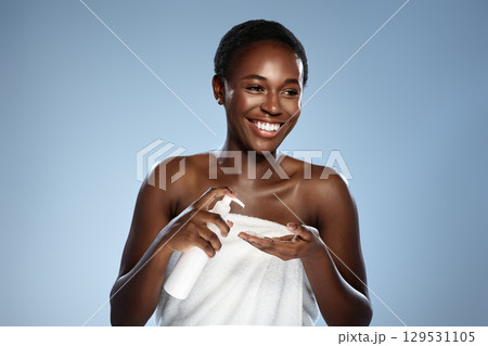 Young woman applying skincare product while smiling against a light blue background in a wellness studio 129531105