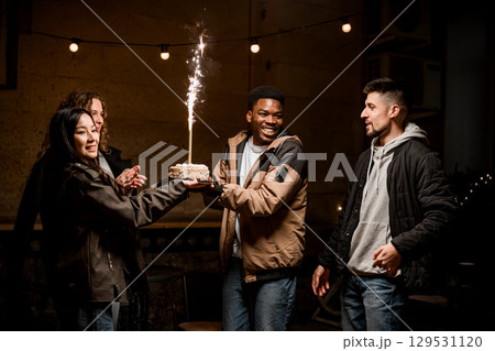 Friends celebrate with cake and sparklers in a cozy indoor gathering at night 129531120