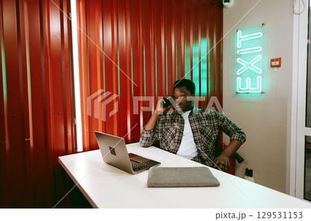 Young man engaged in conversation on the phone while working at a desk in a modern office setting Young man engaged in conversation on the phone while working at a desk in a modern office setting 129531153