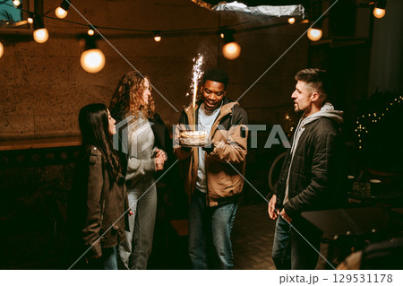 Friends celebrate a birthday outdoors at night with sparklers and festive lights in a lively atmosphere 129531178