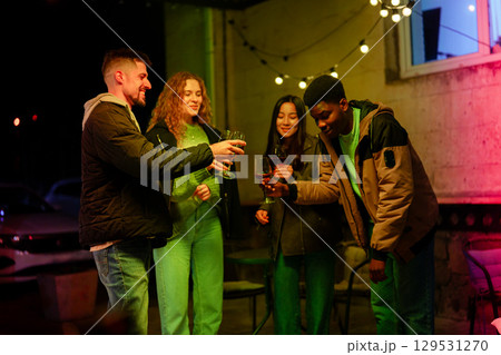 Group of friends celebrating with drinks at an outdoor gathering during a vibrant evening Group of friends celebrating with drinks at an outdoor gathering during a vibrant evening 129531270