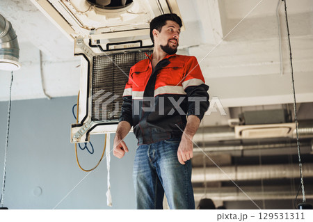 Electrician repairing air conditioning unit in modern commercial space during bright afternoon Electrician repairing air conditioning unit in modern commercial space during bright afternoon 129531311