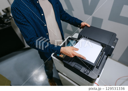 Person using a multifunction printer to copy documents in a modern office environment during daytime hours 129531336