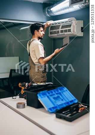 Technician performs maintenance on air conditioning unit in modern office environment during midday 129531338