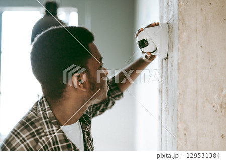Man inspecting security camera installation in modern interior space during daylight hours Man inspecting security camera installation in modern interior space during daylight hours 129531384