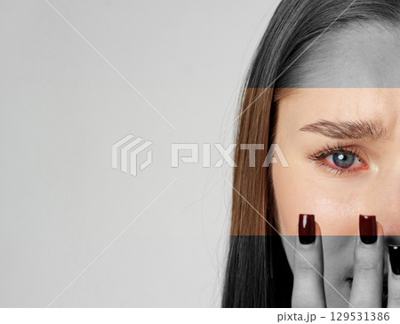 Young woman with long brown hair expressing emotion while covering half her face with her hand in a minimalist setting 129531386