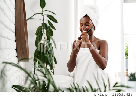 Woman applying skincare product in bright bathroom surrounded by plants in the morning Woman applying skincare product in bright bathroom surrounded by plants in the morning 129531423