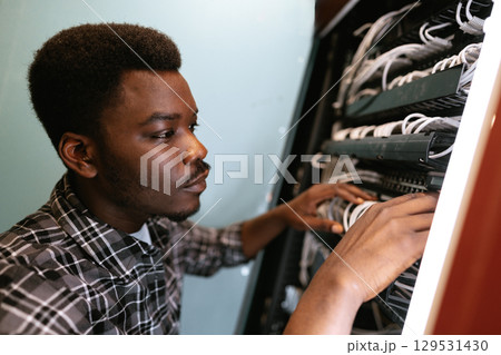 Technician organizing cables in a server room during daylight in a modern office environment 129531430