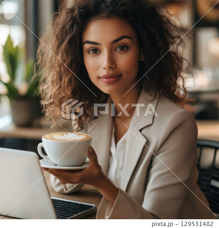 woman in an office, sitting at a desk and enjoying a latte coffee 129531482