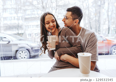 Couple enjoying drinks together, sharing laughter and warmth in a cozy cafe during winter Couple enjoying drinks together, sharing laughter and warmth in a cozy cafe during winter 129531545