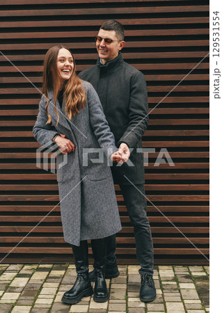Couple enjoying a playful moment outdoors in casual winter outfits against a wooden wall 129531554