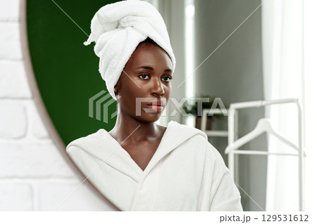 Woman in a white robe and towel gazes in the mirror after a refreshing shower in a cozy bathroom 129531612