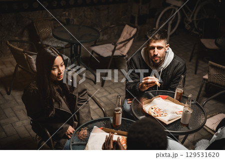 Friends enjoying late-night pizza and drinks at an outdoor cafe in a cozy atmosphere Friends enjoying late-night pizza and drinks at an outdoor cafe in a cozy atmosphere 129531620