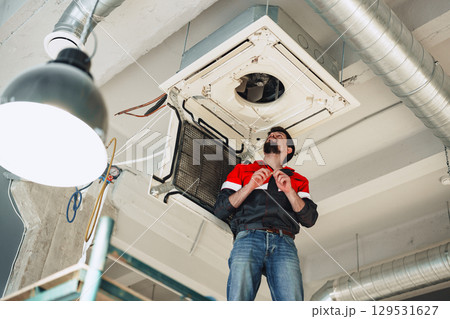 Technician repairs air conditioning unit in modern office space during daylight hours Technician repairs air conditioning unit in modern office space during daylight hours 129531627
