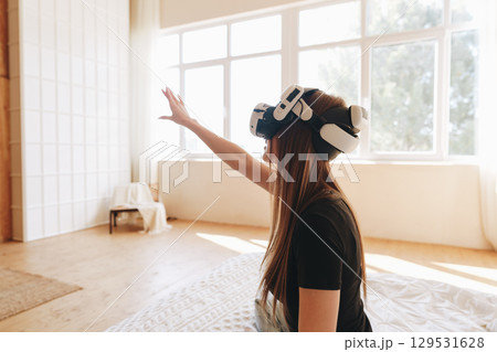 Person experiences virtual reality in a bright room with large windows while reaching out with their hand Person experiences virtual reality in a bright room with large windows while reaching out with their hand 129531628