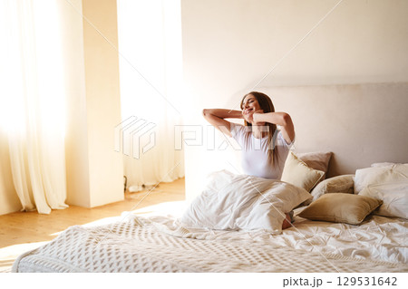 Morning routine in a bright bedroom with a woman stretching and enjoying the sunlight Morning routine in a bright bedroom with a woman stretching and enjoying the sunlight 129531642