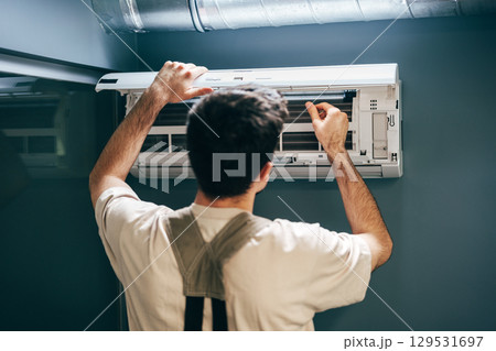 Man performing maintenance on an air conditioning unit in a modern indoor setting 129531697