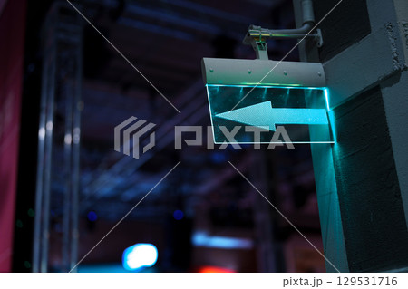 Directional sign illuminated in teal as it guides visitors in an indoor event space during nighttime activities Directional sign illuminated in teal as it guides visitors in an indoor event space during nighttime activities 129531716