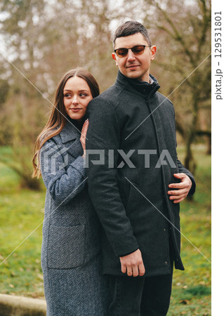 Couple enjoying a cozy moment in a park during a chilly day with lush greenery surrounding them 129531801