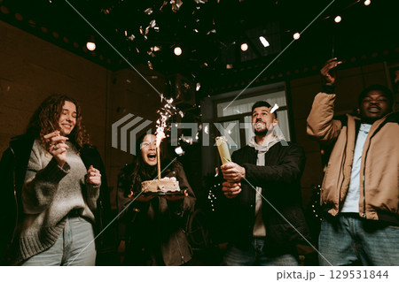 Friends celebrating a birthday with cake, sparkles, and joyful expressions in an indoor party setting Friends celebrating a birthday with cake, sparkles, and joyful expressions in an indoor party setting 129531844