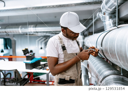 Young technician repairs ventilation system in modern workshop space during daylight hours Young technician repairs ventilation system in modern workshop space during daylight hours 129531854