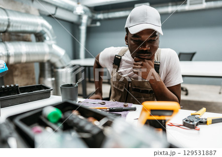 Young man engaged in technical work, analyzing tools and equipment in a workshop environment during daytime Young man engaged in technical work, analyzing tools and equipment in a workshop environment during daytime 129531887