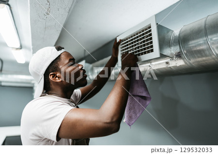 Man cleaning air vent in basement space during daylight hours for better air quality and system maintenance Man cleaning air vent in basement space during daylight hours for better air quality and system maintenance 129532033