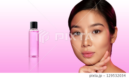 Young woman showcasing skincare product against gradient pink background during a beauty shoot Young woman showcasing skincare product against gradient pink background during a beauty shoot 129532034