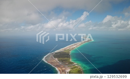 French Polynesia, Rangiroa island: narrow landmass and turquoise water under cloudy sky. Lush greenery borders shoreline, contrast with ocean. Atoll in the Tuamotu Archipelago. Drone flight 129532699