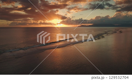 Golden sunset creates a magical atmosphere over the calm ocean waves gently lapping against the shore in Tahiti, French Polynesia, with distant mountains adding to the serene beauty Golden sunset creates a magical atmosphere over the calm ocean waves gently lapping against the shore in Tahiti, French Polynesia, with distant mountains adding to the serene beauty 129532704