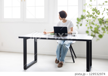 明るい部屋でノートパソコンとノートを使い作業する女性 129532974