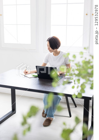 明るい部屋でノートパソコンとノートを使い作業する女性 129532978