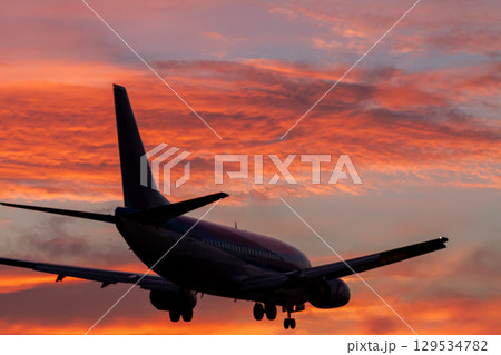 燃える夕焼け空と着陸する旅客機 129534782