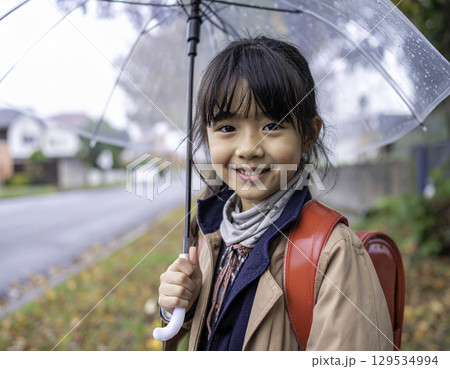 秋の通学路で傘をさしながらやさしく微笑む小学生の女の子（日本人モデル・ランドセル） 129534994