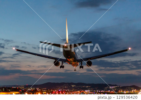 日没した空港に着陸する旅客機 129536420