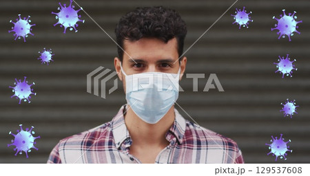 Image of falling covid 19 cells over man wearing face mask 129537608