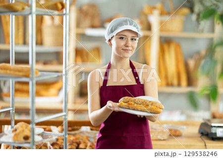 Young woman chef of pastry shop demonstrates product of assortment, bocadillo on disposable plates 129538246