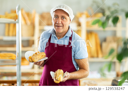 Elderly man chef of pastry shop demonstrates product of assortment, bocadillo on disposable plates Elderly man chef of pastry shop demonstrates product of assortment, bocadillo on disposable plates 129538247