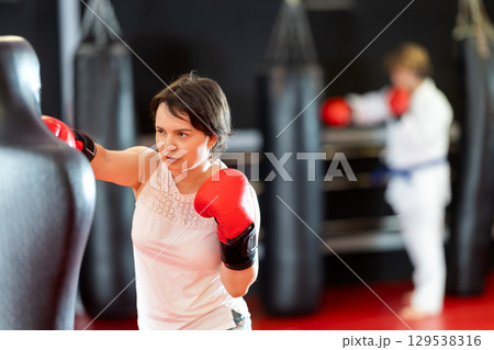 Woman practicing boxing punches on training dummy in gym 129538316