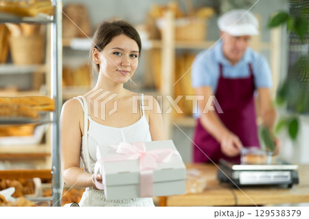 Portrait of young girl buyer with gift box of fresh baked goods in interior of bakery Portrait of young girl buyer with gift box of fresh baked goods in interior of bakery 129538379