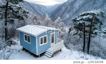 Cozy Blue Cabin Covered with Snow in Winter Forest Surrounded by Snowy Trees and Mountain Valley Landscape 129538599